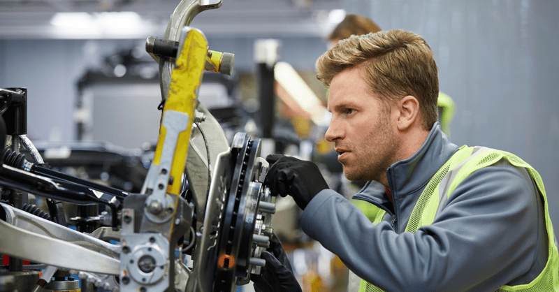 Red-head male automotive factory employee working on an engine part.