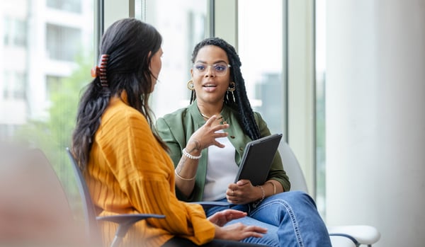 Black female coach, conducting a coaching session with a white woman in a yellow jumper.