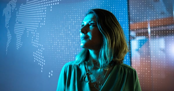 Female business leader standing in front of a hologram of the world and smiling.