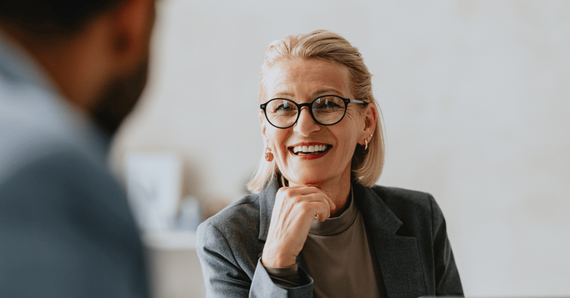 Female senior leader with glasses, smiling in conversation with her coach.