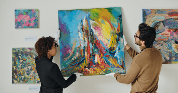 Two gallery curators hanging a piece of vibrant art on the wall.