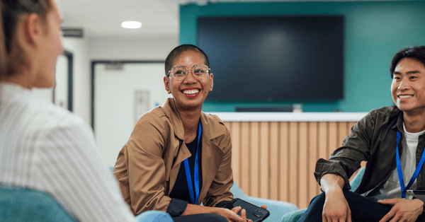 Male and female employees smiling at an unseen third employee while sat down in a group setting.