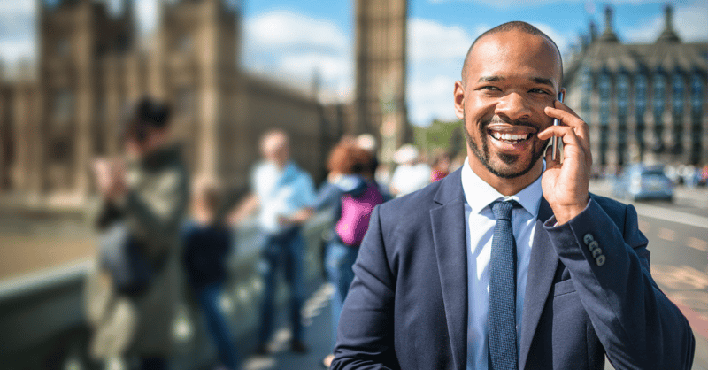 Black, male employee wearing a suit, taking a phone call while walking through London
