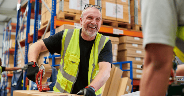 Male warehouse worker in a high-vis vest laughing with colleague as he works.