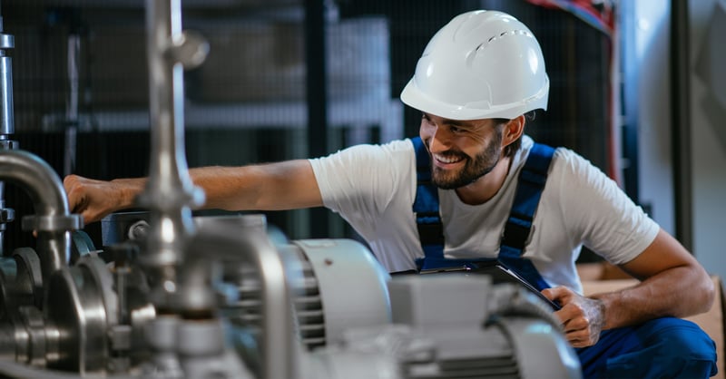 Male metalwork engineer in a white hardhat smiling while working.