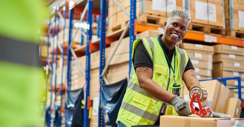 Female packaging employee in factory, smiling at colleague