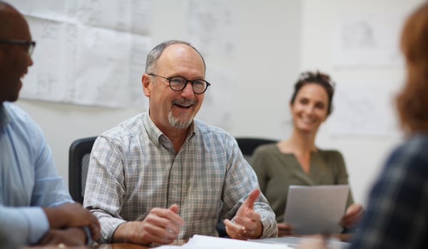 Senior professional in a chequered shirt leading a meeting with colleagues.