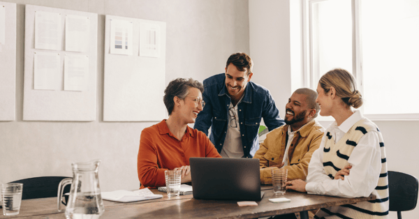 A diverse group of employees sat at a desk, smiling and laughing with each other.