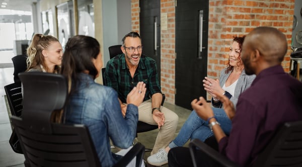 A team of 5 people engaged in a team coaching session, smiling in conversation.