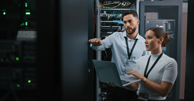 Two employees, one male and one female, in discussion in a server room.